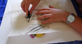Kohlezeichnung Mit Kohlenstift werden unter dem Blatt liegende Blumen durchgepaust