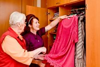 Eine Seniorin und eine Betreuungskraft wählen ein Kleid aus