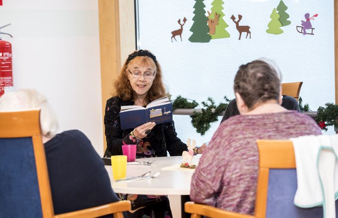 Eine Seniorin liest anderen Senioren aus einem Buch vor