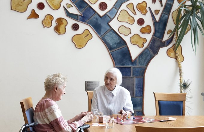 Zwei Seniorinnen sitzen am Tisch und spielen ein Brettspiel