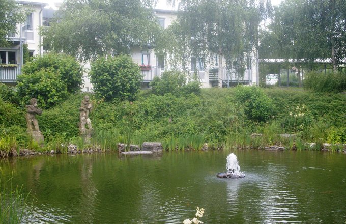 Teich mit Garten und Steinfiguren vor dem Gebäude