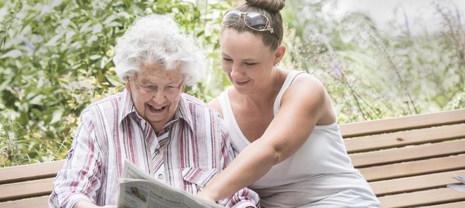 Betreuungskraft und Seniorin schauen Zusammen eine Zeitung an
