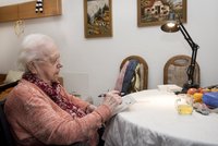 Seniorin sitzt mit Stift in der Hand an einem Tisch