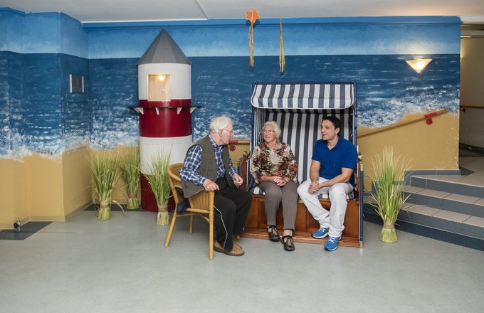 Zwei Personen sitzen in einem Strandkorb, eine auf einem Stuhl daneben