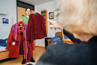 Was wollen Sie anziehen? Pflegerin zeigt Seniorin Kleider für den nächsten Tag Projekt Communicare: Gute Kommunikationsfähigkeiten der Pflegenden im Alltag tragen zum Wohlbefinden der Bewohner oder zuhause Gepflegten bei.