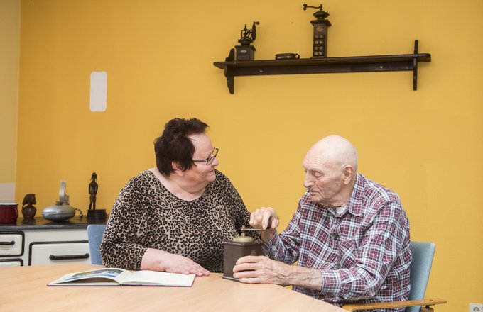 Ehrenamtliche und Senior, der eine alte Kaffeemühle bedient
