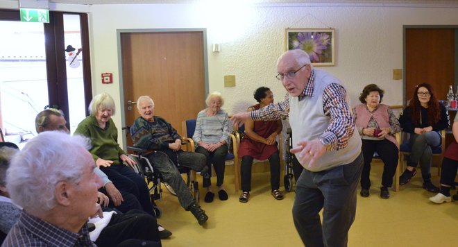 Ehrenamtliches Engagement beim Singkreis. Senioren sitzen im Kreis. In der Mitte steht ein älterer Dirigent.