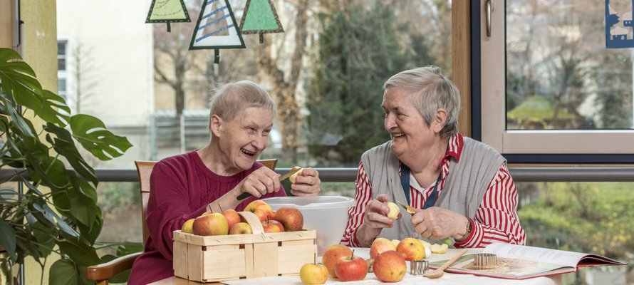 Zwei lachende Seniorinnen schälen gemeinsam Äpfel