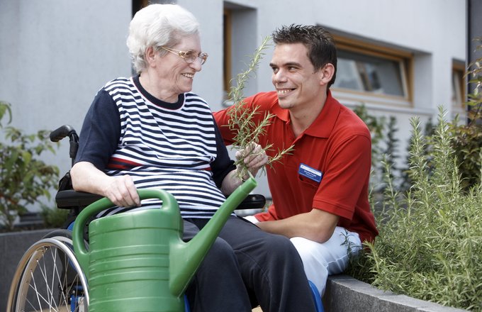 Bewohnerin im Rollstuhl mit Gießkanne und Mitarbeiter