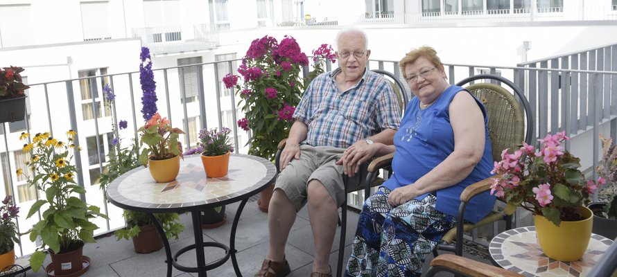 Ein älteres Paar sitzt zwischen Blumen auf seinem Balkon.