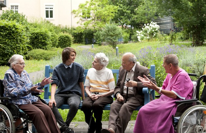 Vier Senioren und ein junger Mann sitzen gemeinsam im Garten des Ludwigstifts