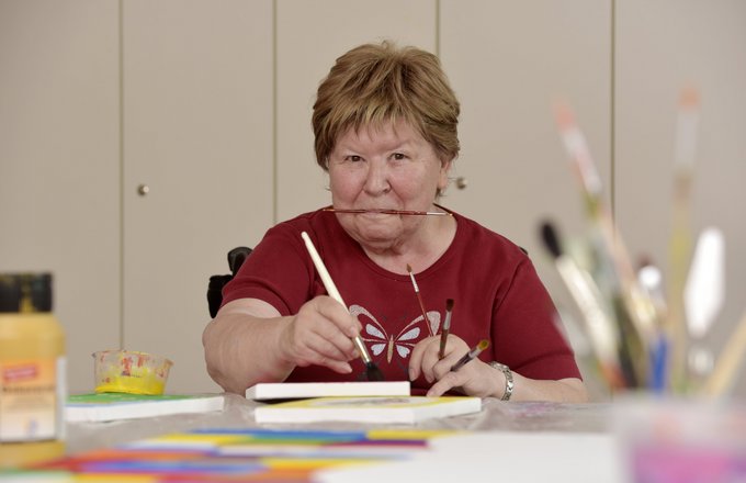 Seniorin malt, einen weiteren Pinsel zwischen den Zähnen haltend