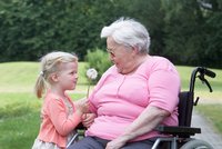 Kleines Mädchen überreicht Seniorin im Rollstuhl eine Pusteblume