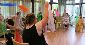Inhouse-Schulung im Altenburgheim Frauen sitzen im Kreis auf stühlen und schwingen bunte Tülltücher