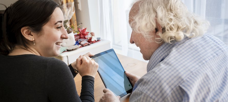 Eine junge Frau und ein Senior bedienen zusammen einen Tablet-Computer