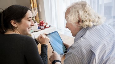 Eine junge Frau und ein Senior bedienen zusammen einen Tablet-Computer